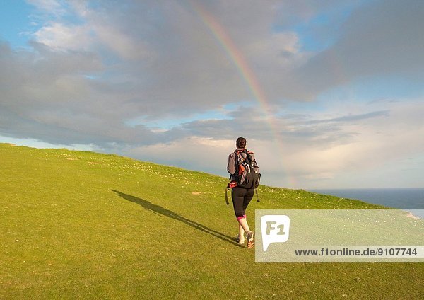 Junge Wanderin wandert bergauf Richtung Regenbogen