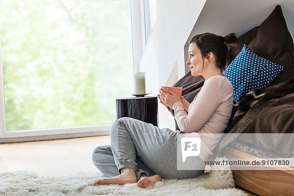 Mittlere erwachsene Frau auf dem Boden sitzend mit Kaffee