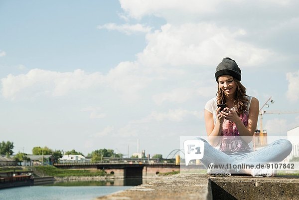 Young woman sitting on wall using cell phone
