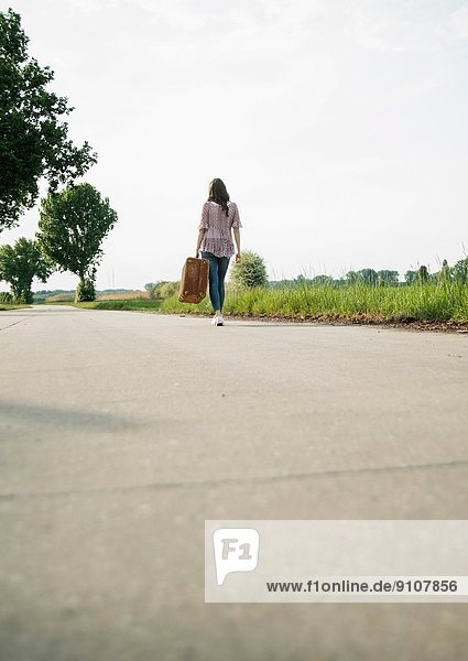 Young woman walking on country road carrying suitcase