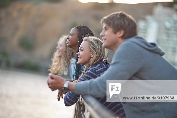 Vier junge erwachsene Freunde  die von den Geländern am Flussufer blicken.