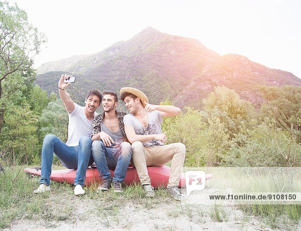 Three young men sitting on top of canoe  taking self portrait photograph