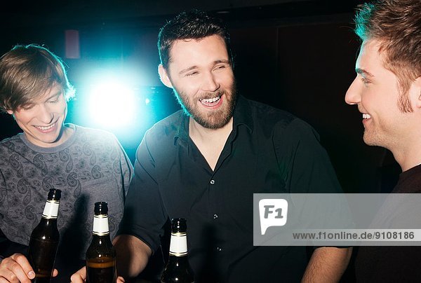 Three male friends drinking bottled beer in nightclub