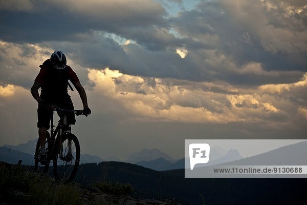 A male mountain biker riding at ridgetop at sunset. Canmore  Alberta  Canada
