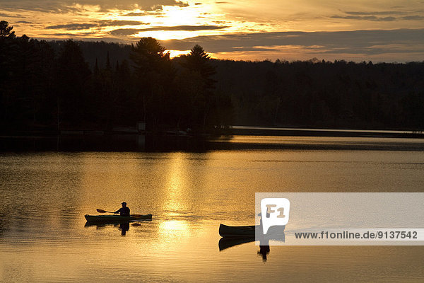 Two men paddle canoe and kayak on Oxtongue Lake at sunrise  Muskoka  Ontario  Canada.