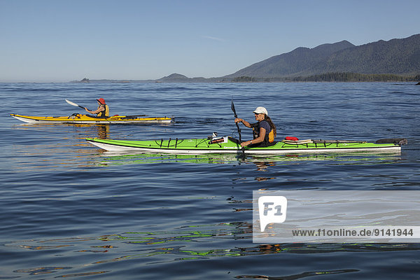 Two female kayakers paddle off Flores Island Provincial Park in Clayoquot Sound British Columbia Canada. Model Released