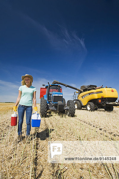 a farm girl standing in oat stubble in front of a tractor  grain wagon and combine during the harvest  near Dugald  Manitoba  Canada
