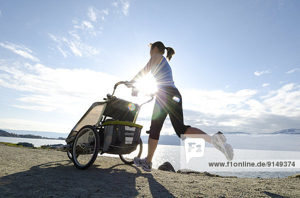 A woman jogs on the shores of Okanagan Lake with her baby in a child carrier