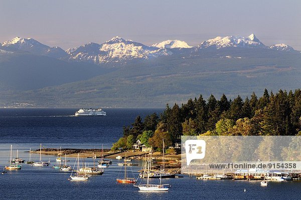 Boats anchored in the bay by Protection Island near Nanaimo  BC. The BC Ferry Queen of Cowichan sails to Vancouver with the mountains on the mainland of British Columbia in the background.