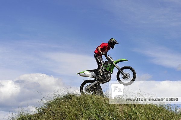 A motorcycle rider landing a jump on top of the dirt hill at a motocross event in Alberta Canada