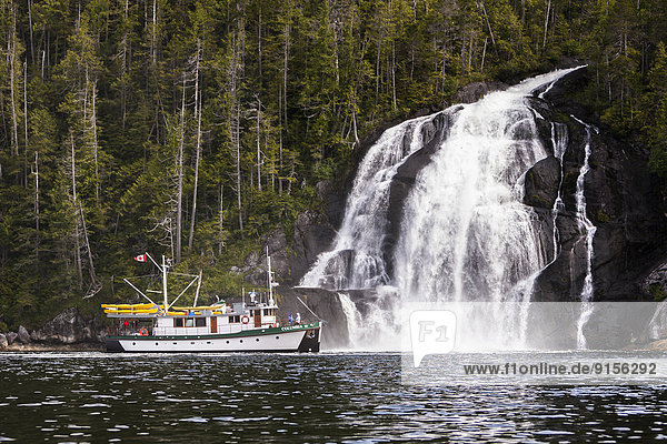 Columbia III steams alongside a cascading waterfall while traveling through Kynoch Inlet on British Columbia's Northern Coast. Fjordland  Great Bear Rainforest  Northern British Columbia Coast  British Columbia  Canada.