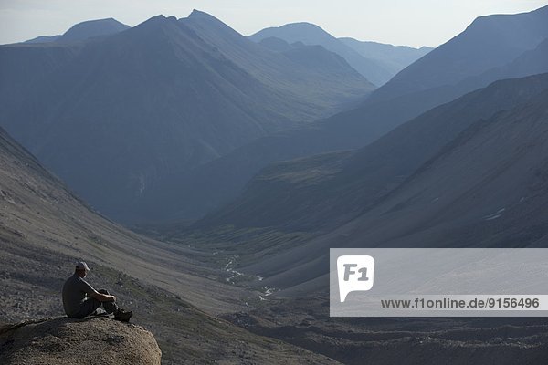man sitting on a rock overlooking Jones Pass in the Yukon Coast Mountains.