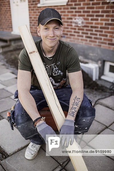 Porträt eines lächelnden Zimmermanns mit Holzbrettern auf der Baustelle
