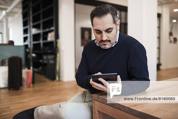 Mittlerer erwachsener Geschäftsmann mit digitalem Tablett am Schreibtisch im Büro