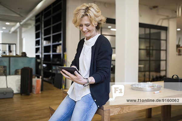 Reife Geschäftsfrau mit digitalem Tablett am Schreibtisch im Büro