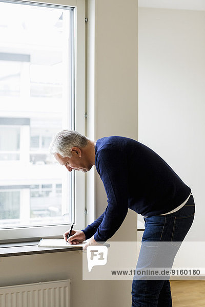 Side view of businessman writing at window sill at home
