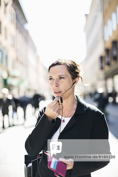 Mature businesswoman talking through headphones on city street