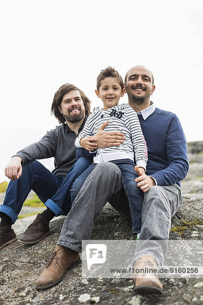 Portrait of happy male homosexual family relaxing on rock
