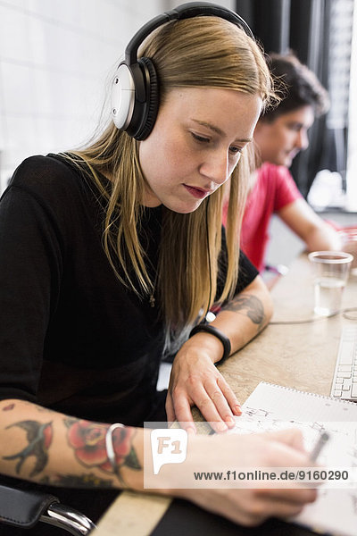 Junge Geschäftsfrau mit Kopfhörer beim Schreiben im neuen Büro