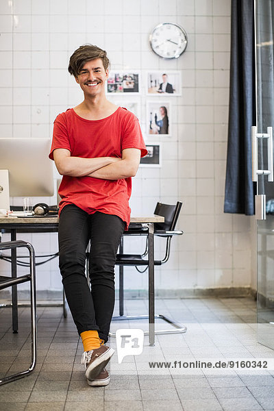 Full length portrait of smiling young businessman with arms crossed in new office