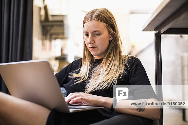 Junge Geschäftsfrau  die im kleinen Büro auf einem Laptop sitzt.