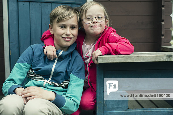Porträt eines behinderten Mädchens mit Arm um den Bruder auf der Veranda sitzend