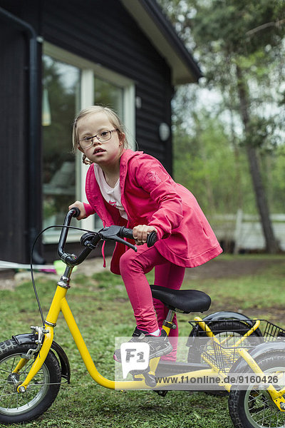 Portrait of girl with down syndrome riding bicycle in lawn