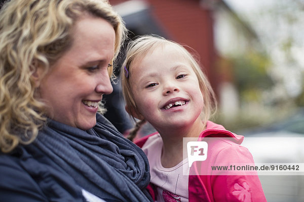 Porträt eines glücklichen Mädchens mit Down-Syndrom  getragen von der Mutter