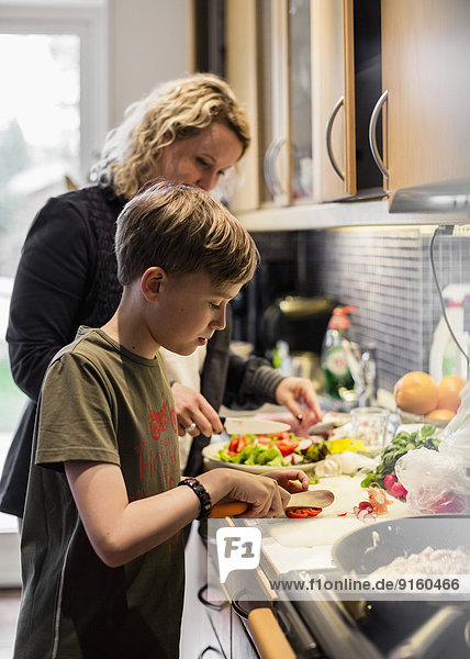Sohn und Mutter schneiden Gemüse in der Küche