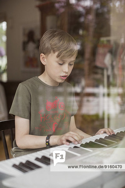 Junge signiert beim Klavierspielen im Haus