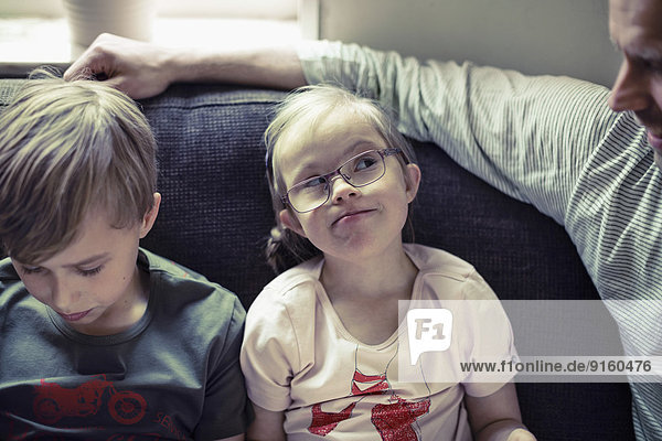 Mädchen mit Down-Syndrom betrachtet Vater von Bruder auf Sofa