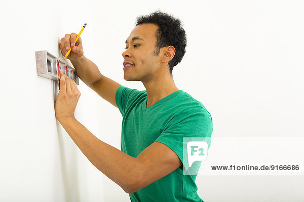 Mixed race man using level on wall