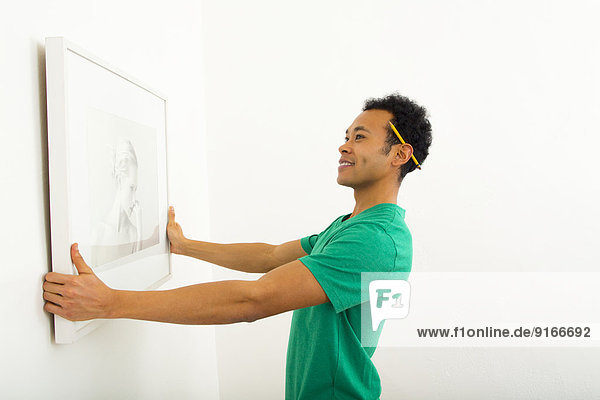 Mixed race man hanging picture on wall