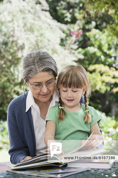 Grandmother reading to granddaughter outdoors