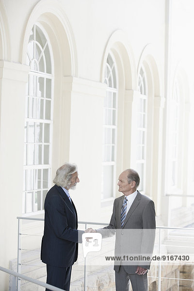 Senior Caucasian businessmen shaking hands on balcony