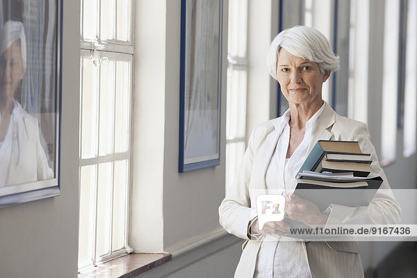 Senior Caucasian businesswoman carrying books in office