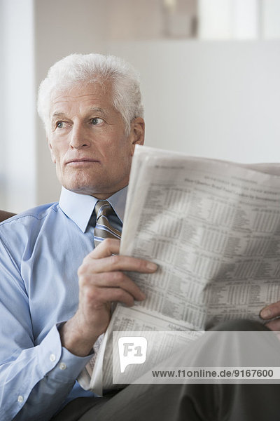 Caucasian businessman reading newspaper in office