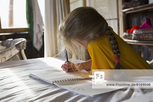 Caucasian girl drawing in notebook on bed
