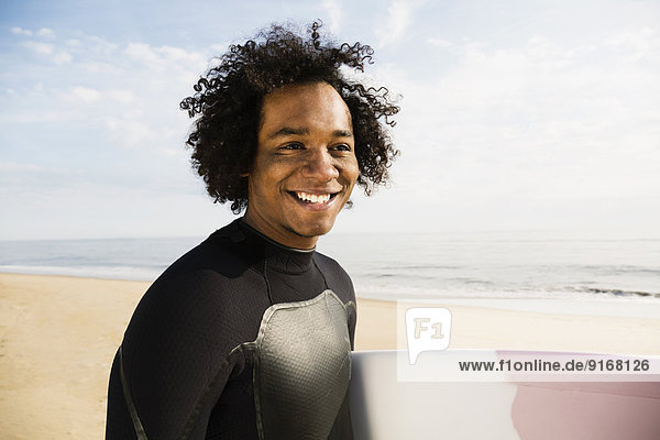 Mixed race surfer carrying board on beach