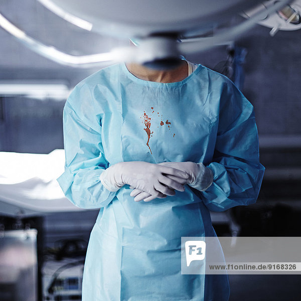 Caucasian surgeon with blood on gown in operating room
