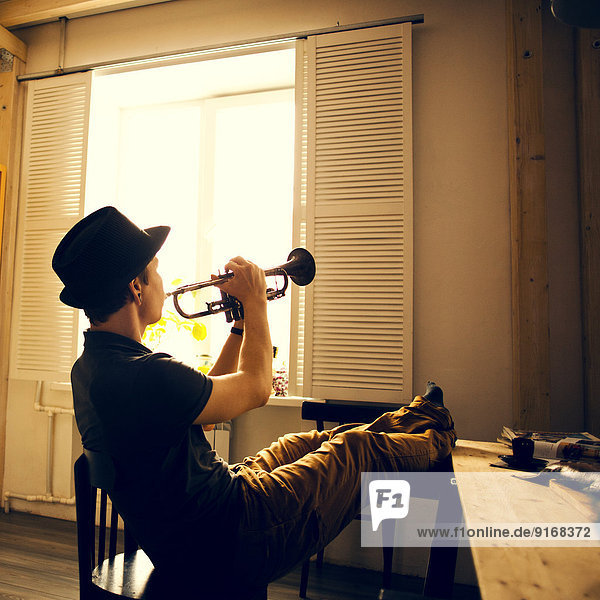 Caucasian man playing trumpet in kitchen