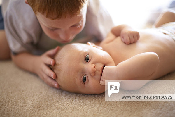 Caucasian boy kissing baby brother on carpet