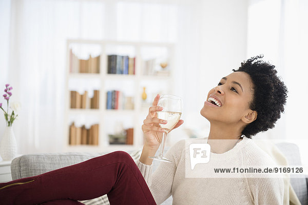 Black woman drinking wine on sofa