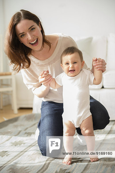 Mother helping baby stand in living room