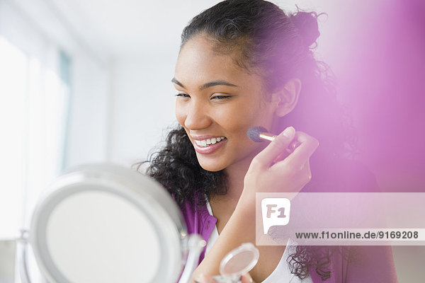 Mixed race woman applying makeup in mirror