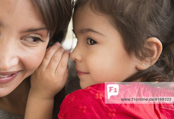 Hispanic girl whispering in mother's ear