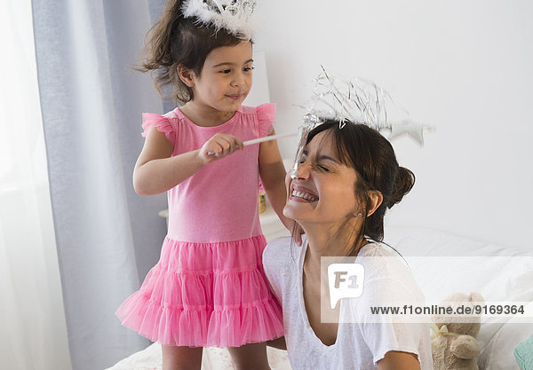 Hispanic mother and daughter playing dress up on bed