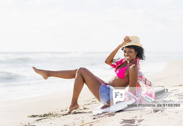 African American woman sitting on surfboard on beach