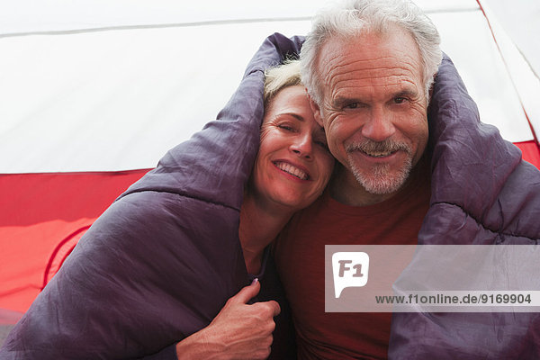 Senior Caucasian couple in sleeping bag in tent