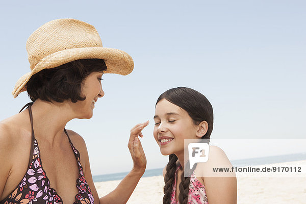 Mother rubbing sunscreen on daughter on beach